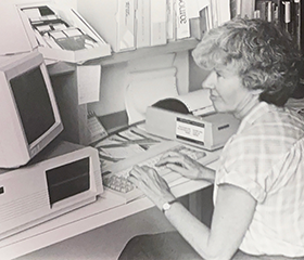 Black and white photo of Jean Tague Sutcliffe sitting at a desktop computer