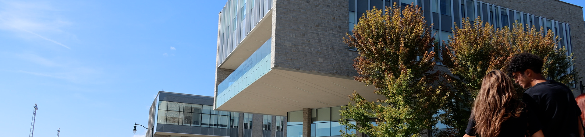 An extreior image of the FIMS and Nursing building. The sky is bright blue and students are walking across the street towards the building.