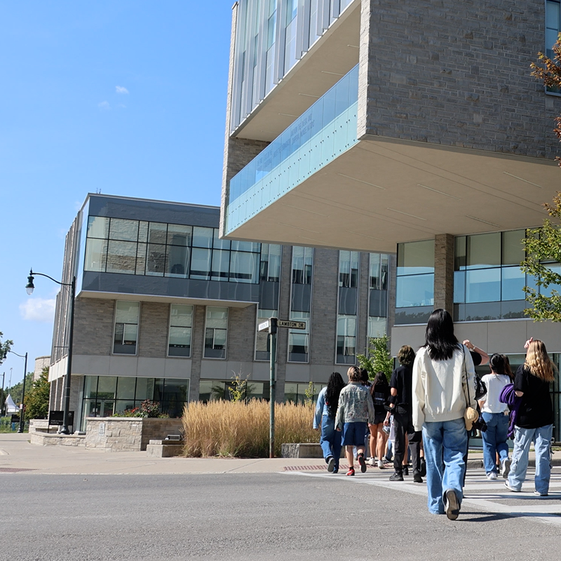 An extreior image of the FIMS and Nursing building. The sky is bright blue and students are walking across the street towards the building.