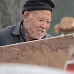 Man outside wearing a toque and holding wood.