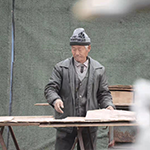 Man outside wearing a toque and working with wood on a table.