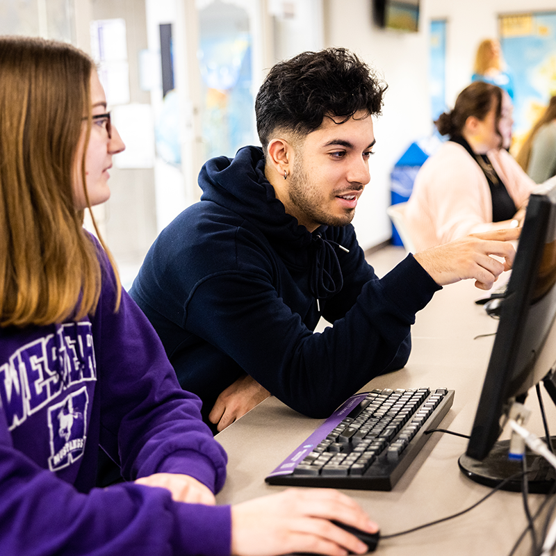 Two students sit and look at a computer together