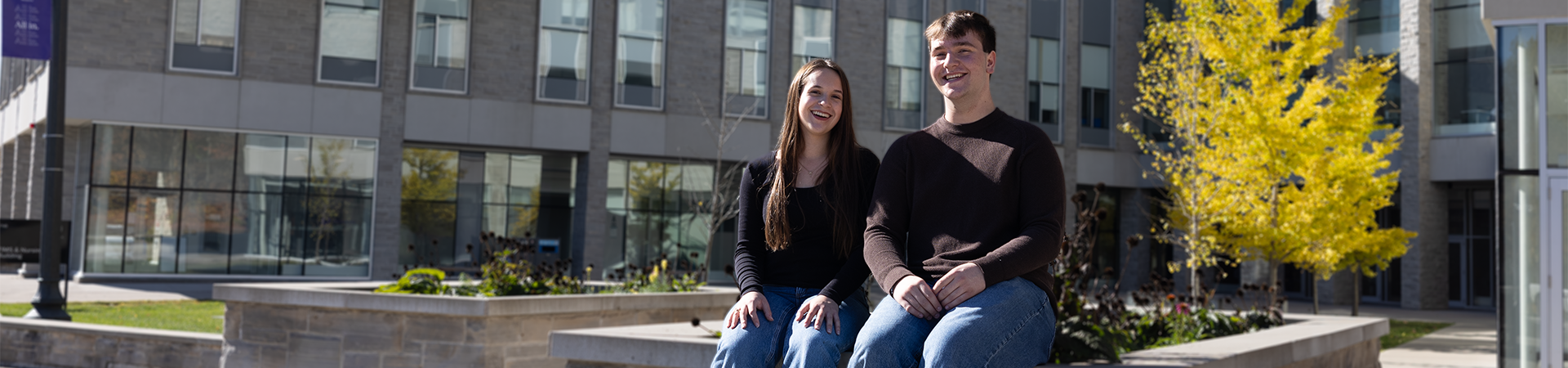 Two students sitting outside of the FIMS & Nursing Building on a sunny day