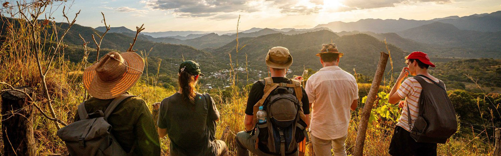 Several researchers with backpacks survey a small town from a hill top in El Salvador. The sun is setting. Photo by Shawn Robertson in 2023 in El Salvador
