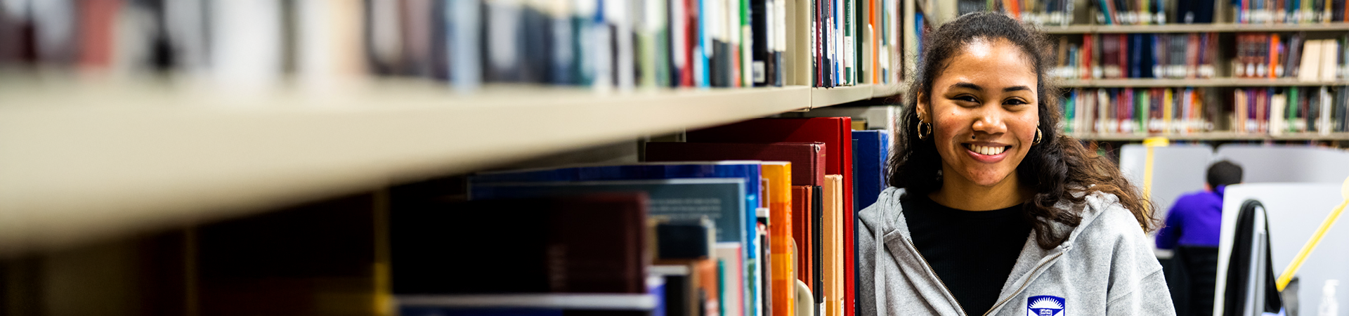 A young female student posing beside a row of books