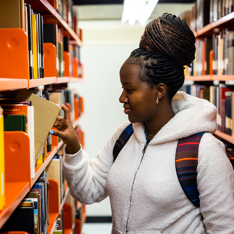 A young black woman pulling a book off of a bookshelf