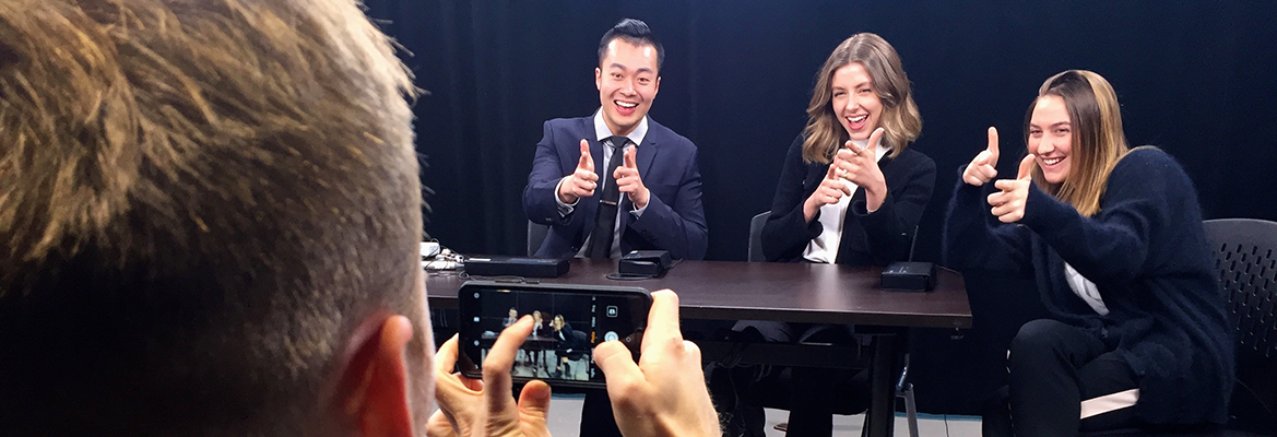 Three students in the broadcast studio being filmed by a fourth student.