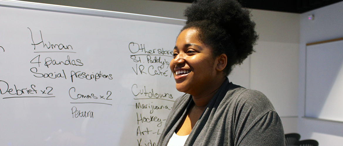 A student laughs while standing in front of a whiteboard in the newsroom