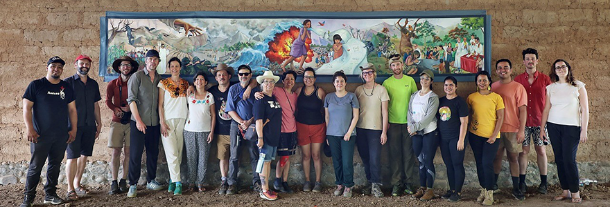 Members of the Surviving Memory in Postwar El Salvador research team stand in front of a mock-up draft of a collaborative mural in 2025 at the site of the Sumpul River Massacre (Photo: Filip Desjardins)