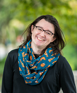 Headshot of Professor Bri Watson standing outside against a green backdrop of foliage.