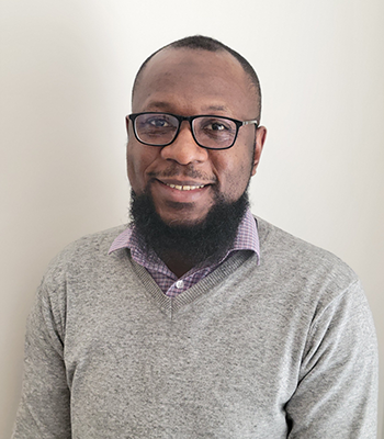 Abdul Sulley wearing a grey sweater and purple and white-checked button down shirt