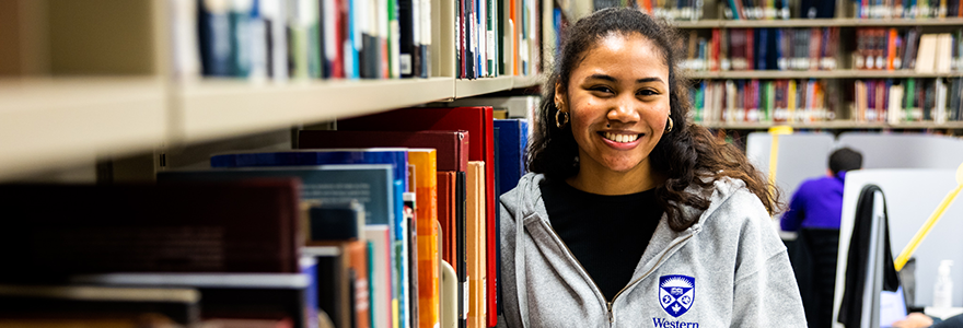 A student in a Western hoodie stands among library stacks