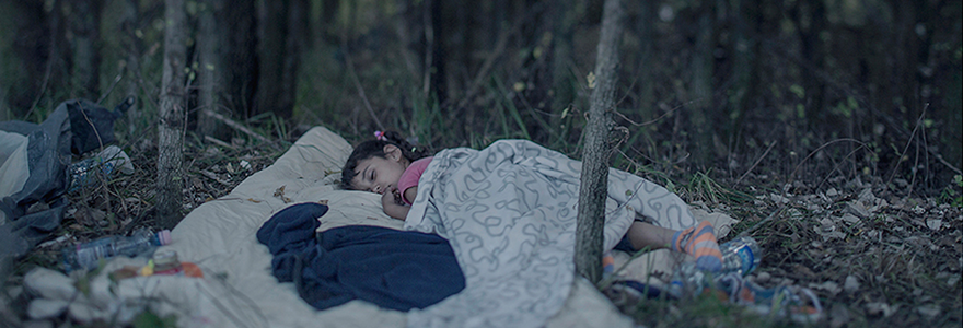A child sleeping under a blanket on the floor of a forest.
